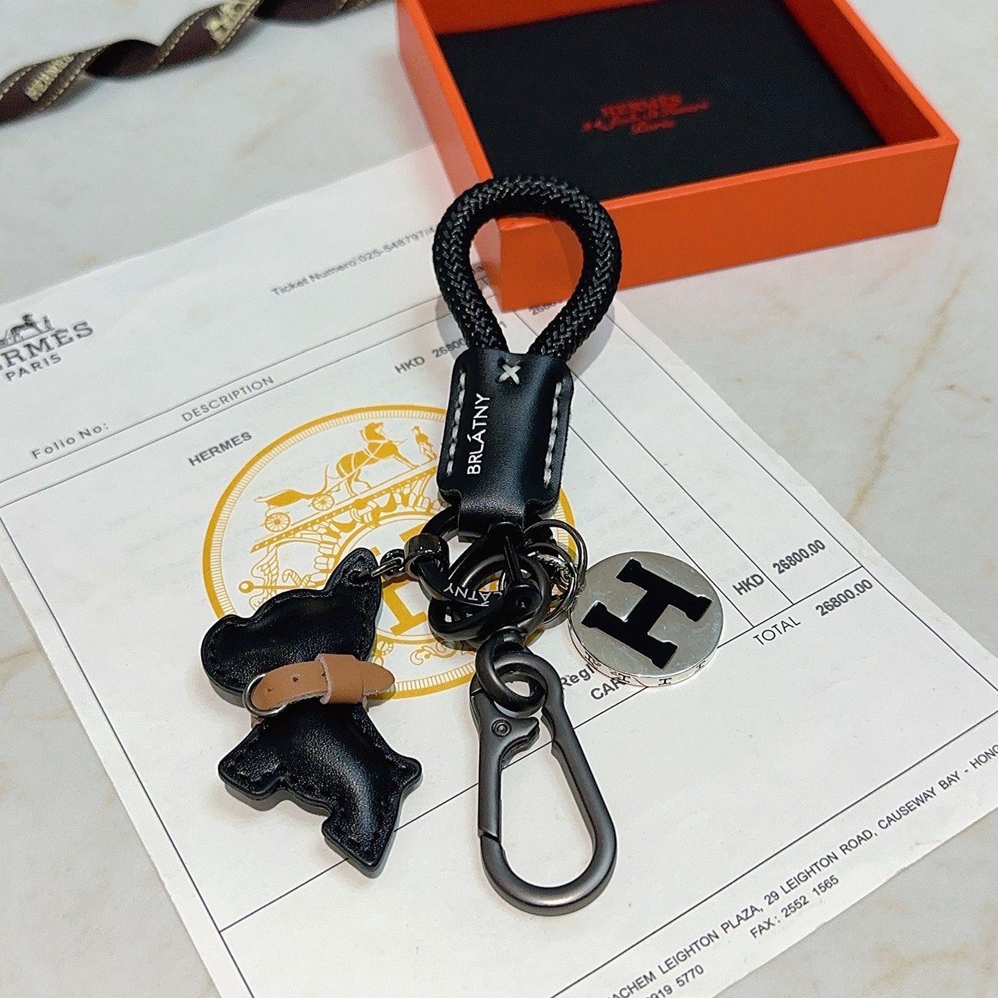 Hermes H Logo Bulldog Charm Chaveiro pingente Cordão trançado preto Couro preto com detalhes em couro bronzeado Hardware em metal prateado com esmalte preto Logotipo H 12 cm de comprimento total